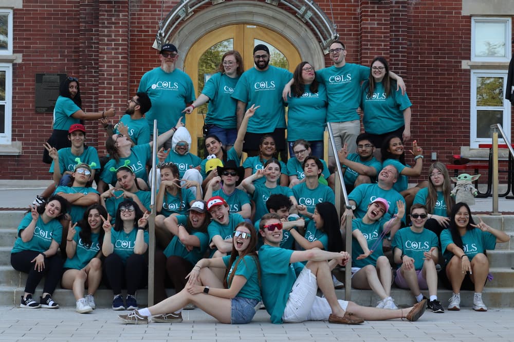 COLS volunteer staff in teal T-shirts posing on stone steps, a few stretched out across the front row