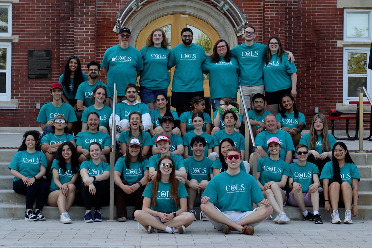 COLS volunteers in matching teal T-shirts posing together on the steps of a red-brick building