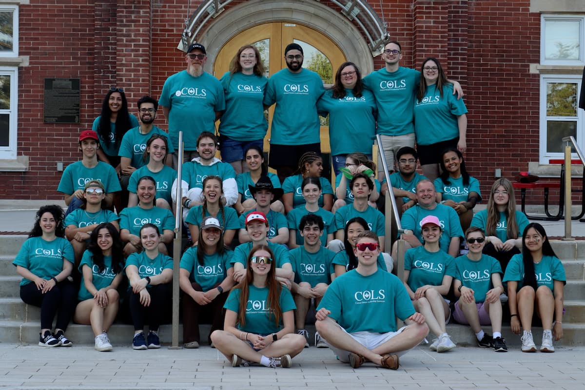 COLS volunteers in matching teal T-shirts posing together on the steps of a red-brick building