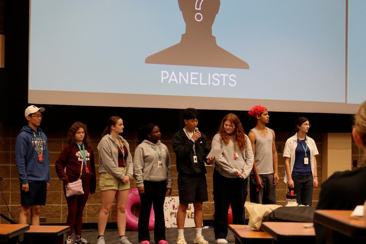 A row of COLS ambassadors standing on stage under a screen that reads Panelists