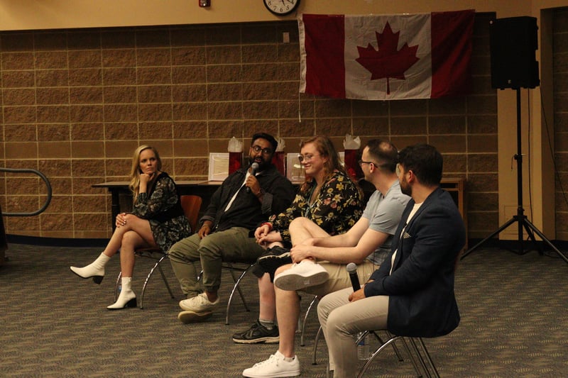 Four panelists seated in a row beneath a Canadian flag, talking with ambassadors