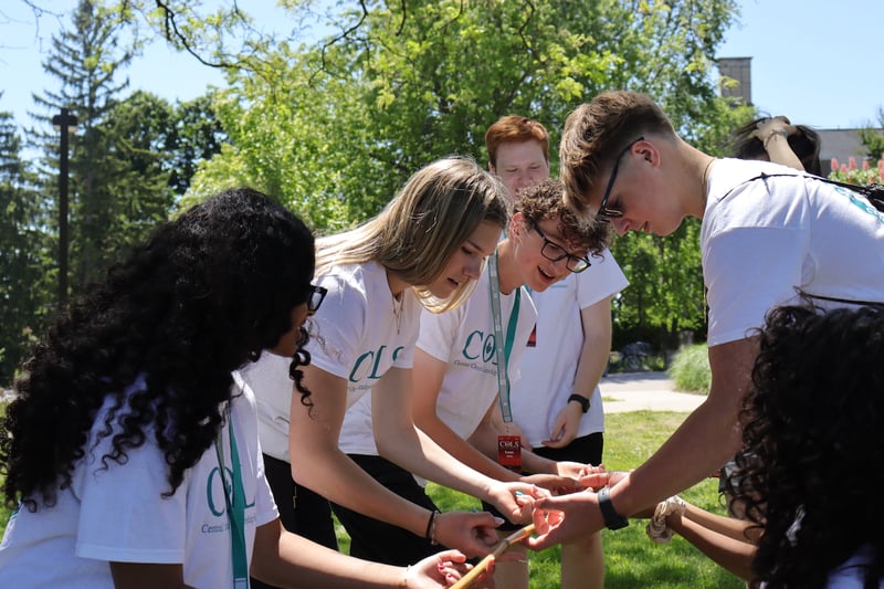 Ambassadors in white COLS T-shirts huddled together outdoors, hands joined in a team-building challenge