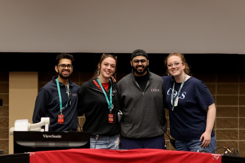 Four COLS team members wearing lanyards, smiling together on stage