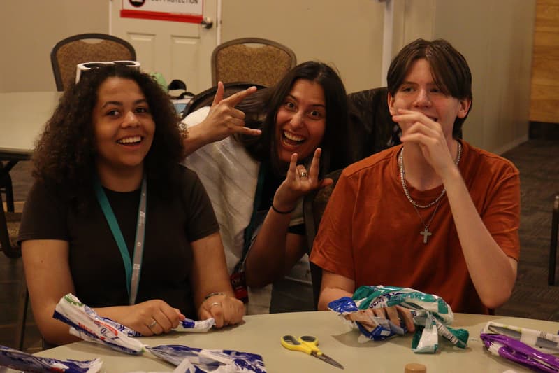 Three ambassadors smiling at a craft table, one making a peace sign